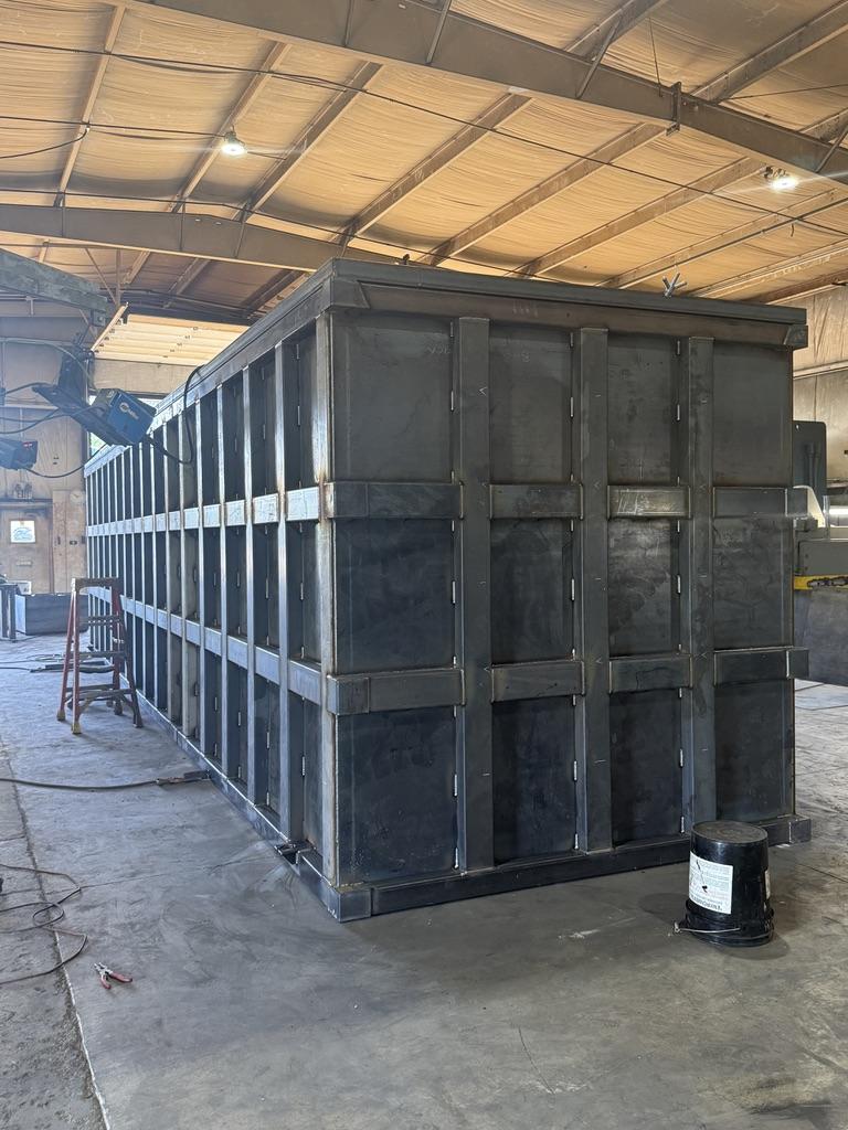 Bare carbon-steel EnviroBox shell under fabrication on the shop floor showing full-height rib bracing