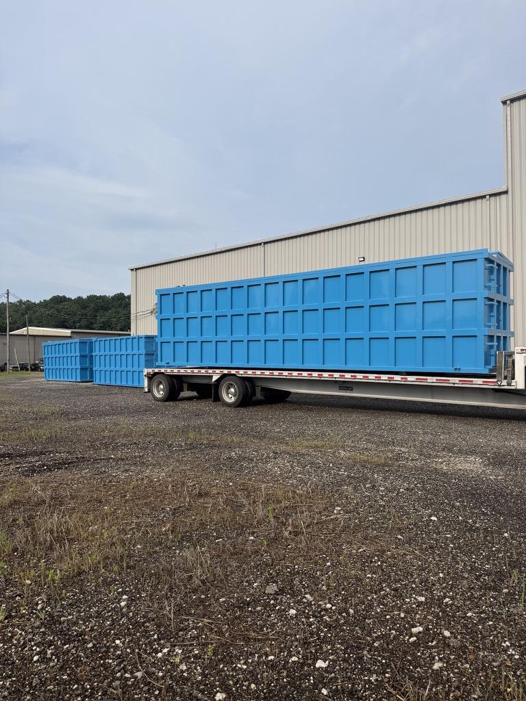 Blue EnviroBox tank loaded on a flatbed trailer beside the shop building